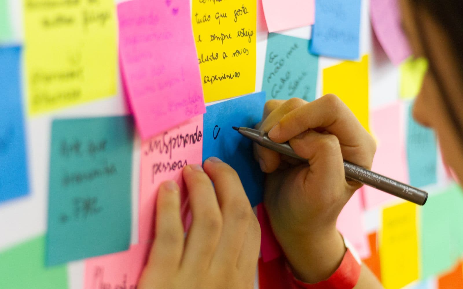 A hand writing ideas on colourful sticky notes stuck to a wall