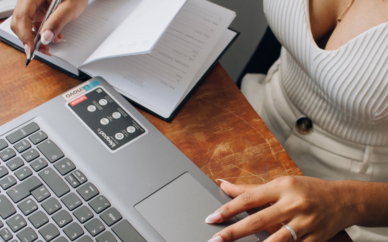 Close-up of a woman writing notes in a notebook beside her laptop