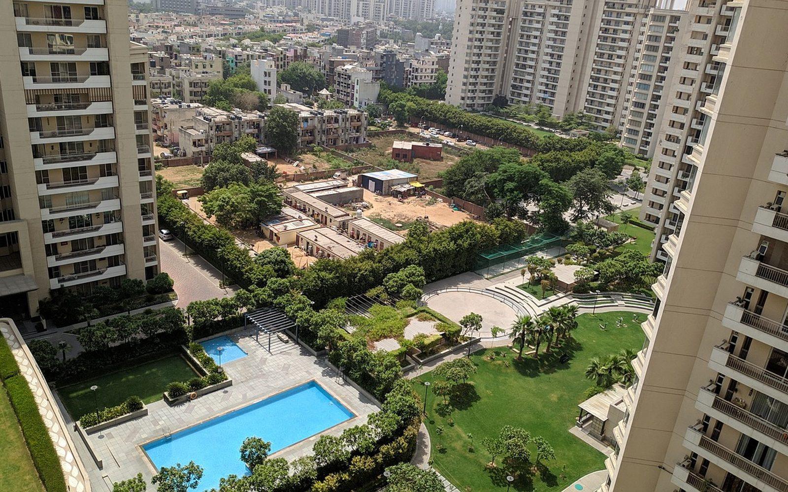 High-rise residential towers in Gurugram around a garden and swimming pool, seen from above