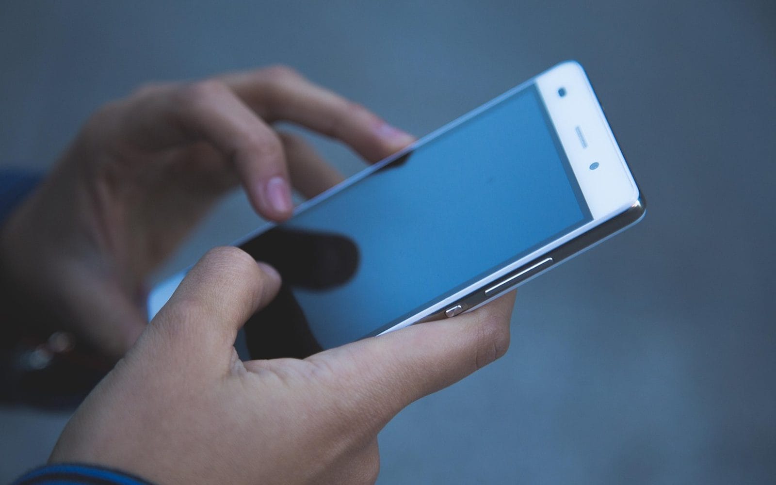 Close-up of two hands typing on a smartphone against a blue background
