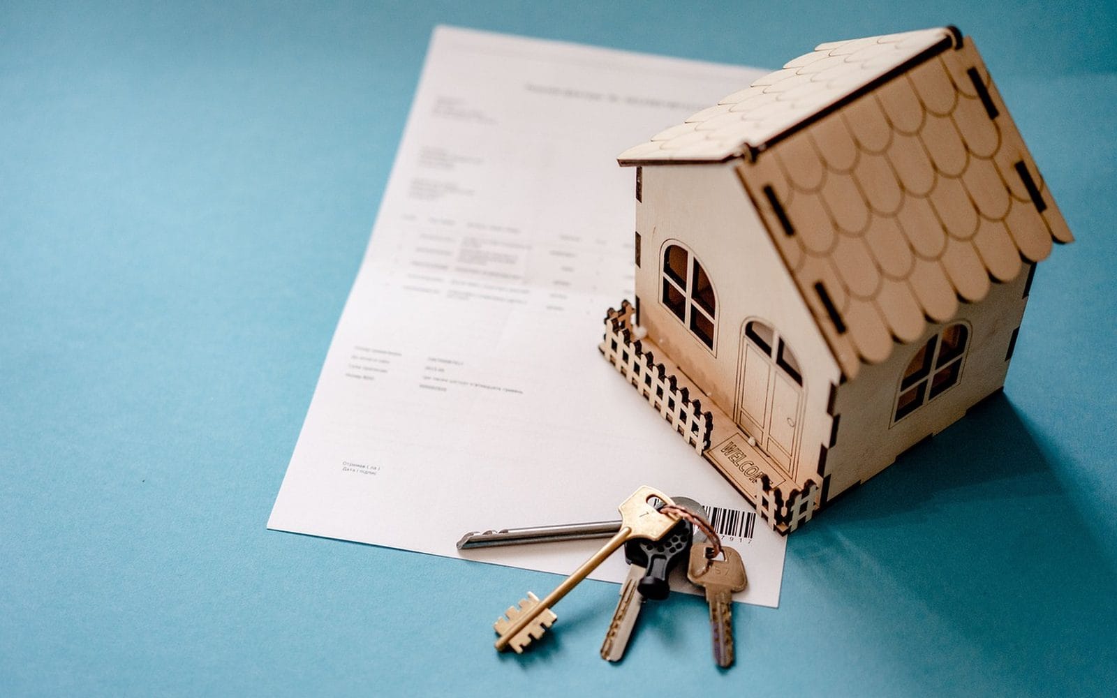 A small wooden house model on a printed agreement with a set of keys beside it