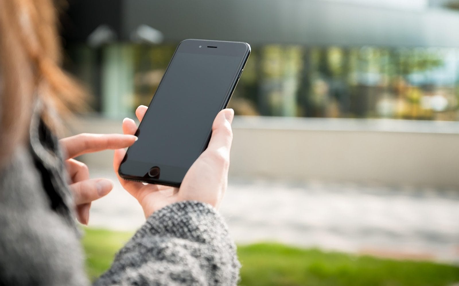 A woman holding a smartphone outdoors and tapping the screen