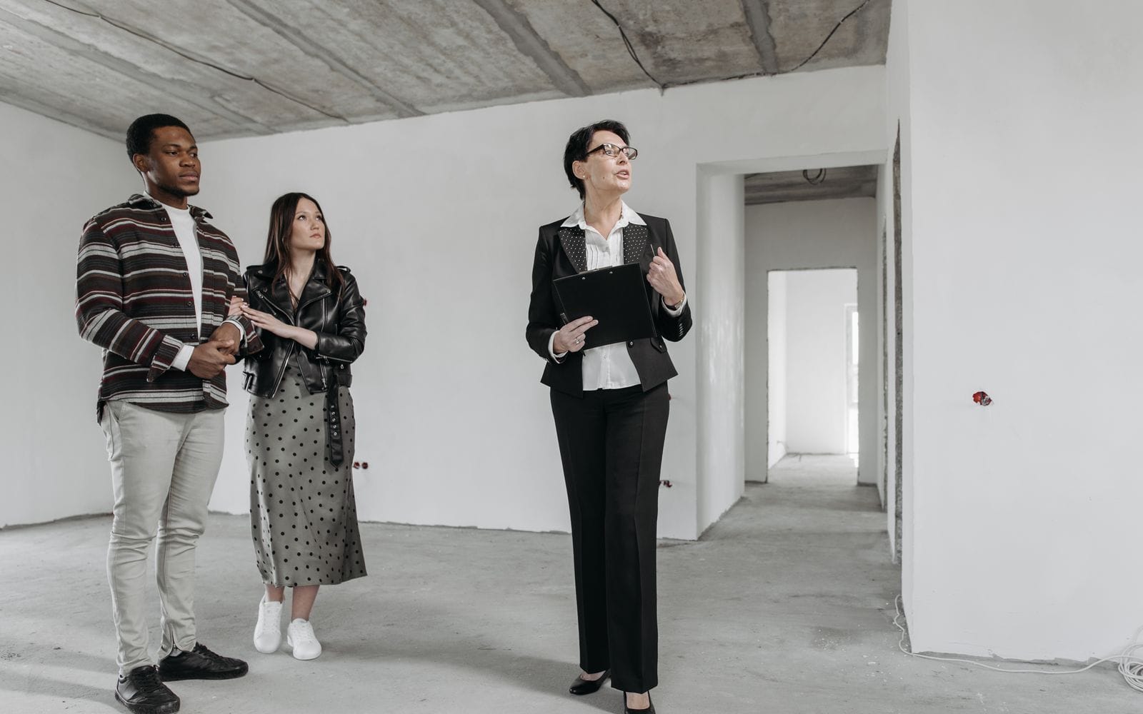 A real estate agent with a clipboard showing an unfinished flat to a young couple