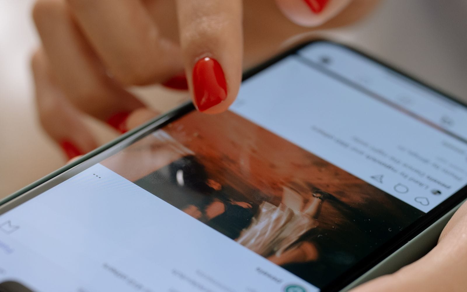 Close-up of a hand with red nails scrolling a social media feed on a phone