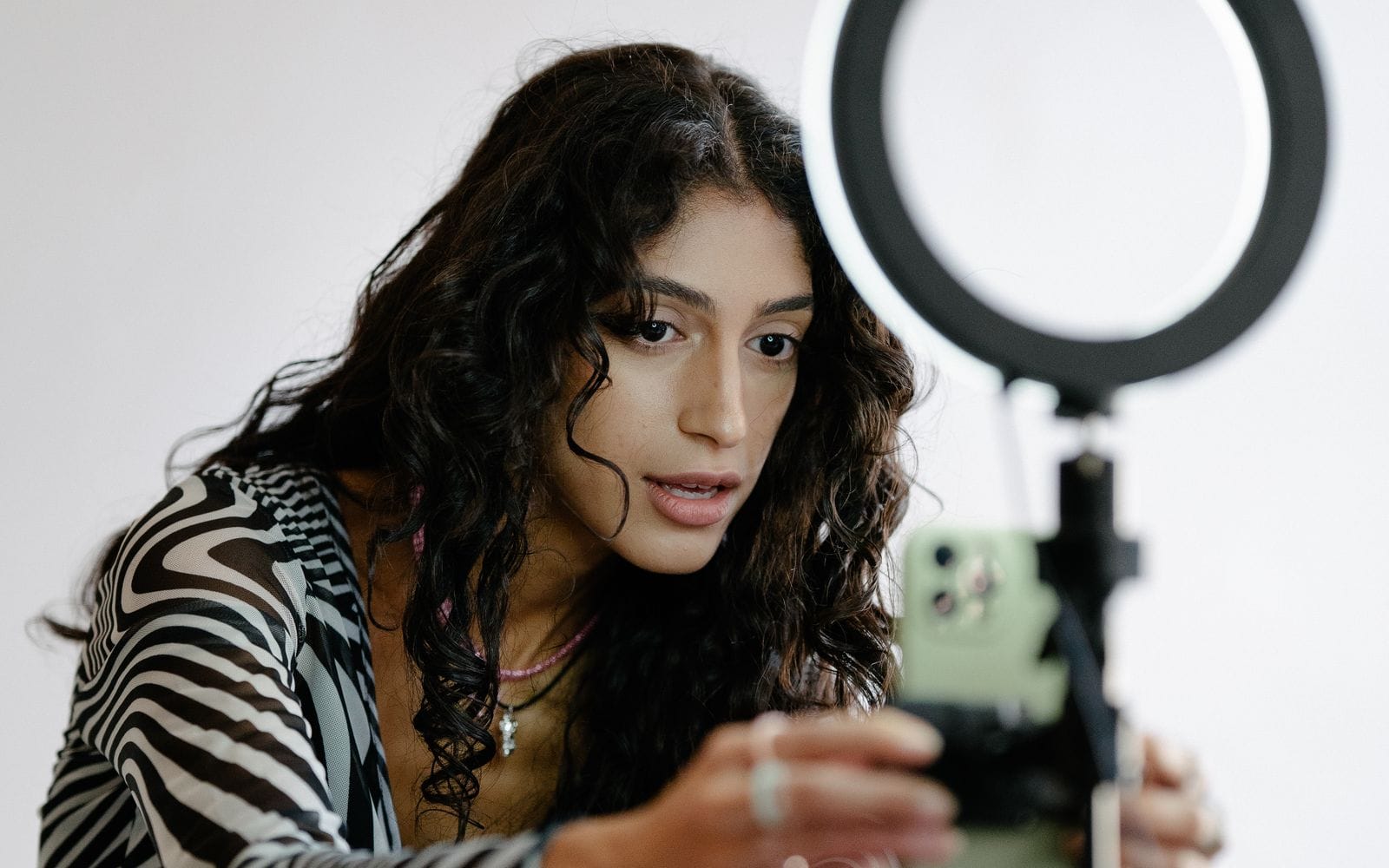 A woman adjusting a smartphone on a tripod in front of a ring light