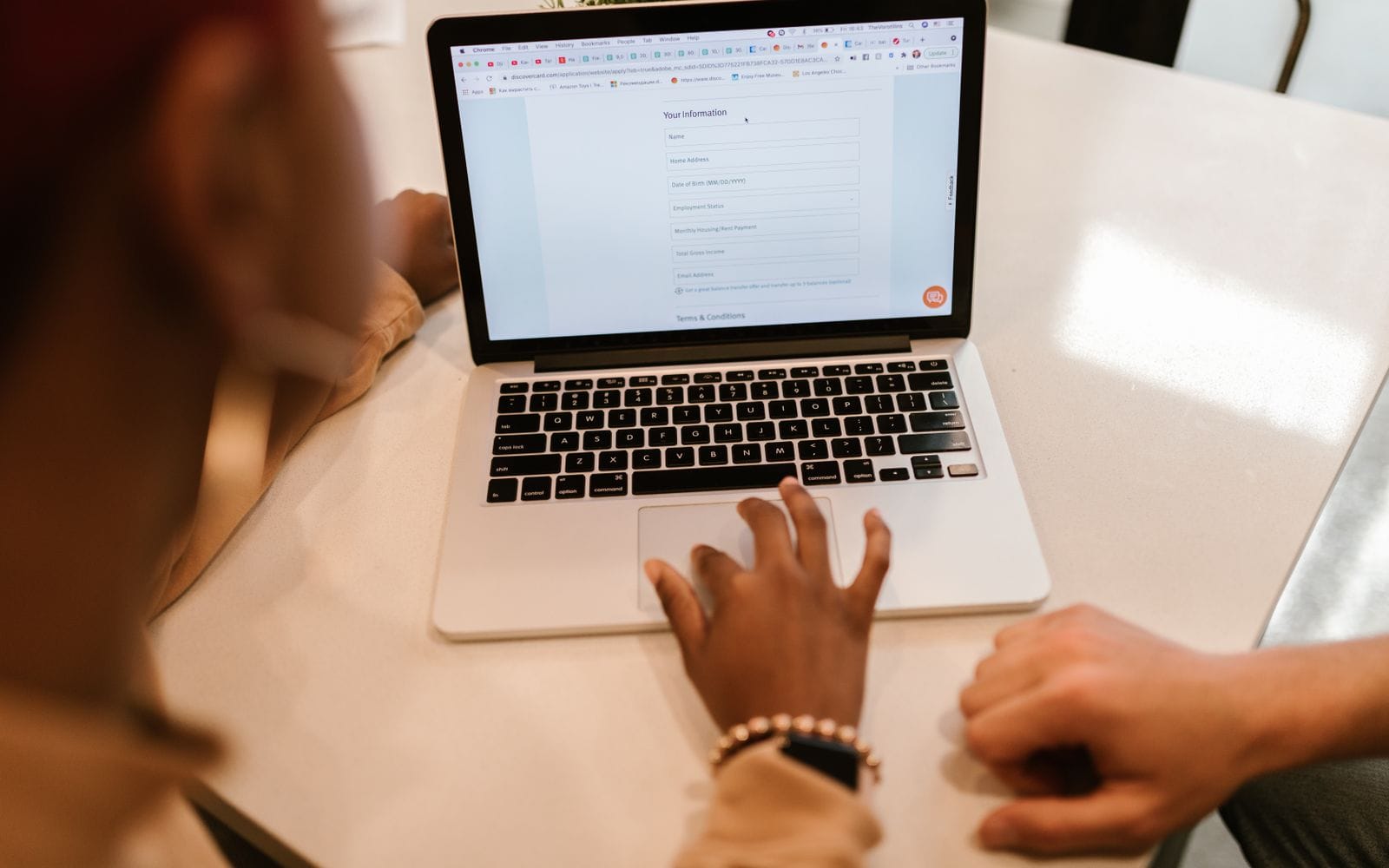 Two people at a white table filling in an online form on a laptop