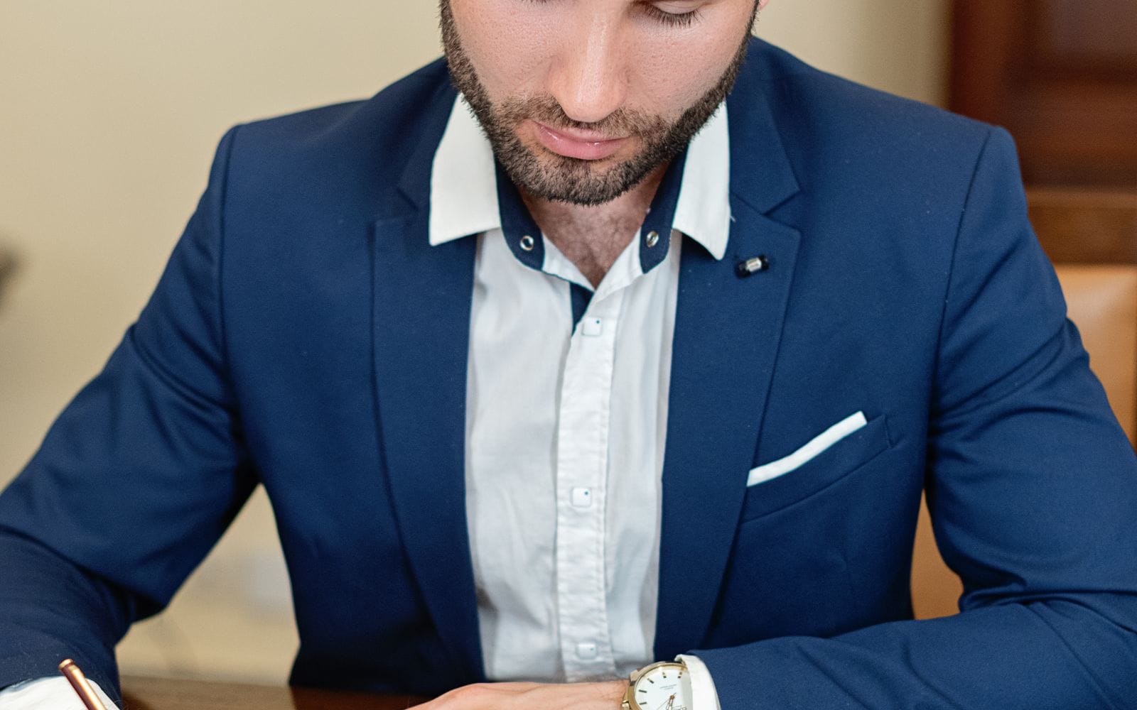 A man in a navy suit reading a document at his desk