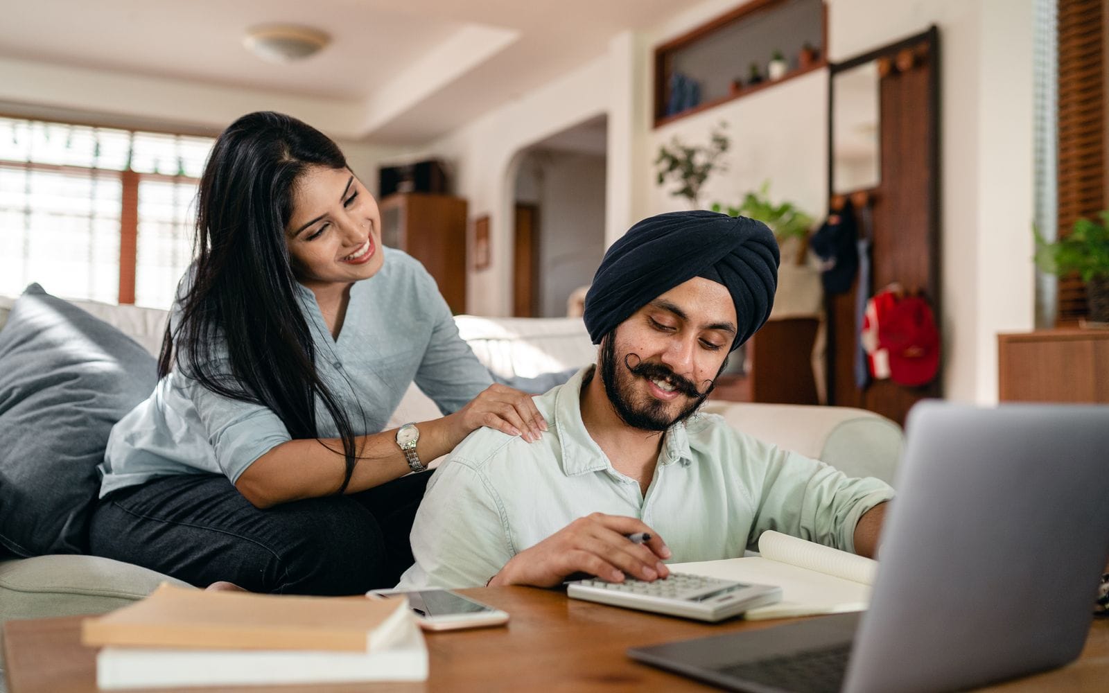 A couple at home checking papers with a laptop, phone and calculator on the table