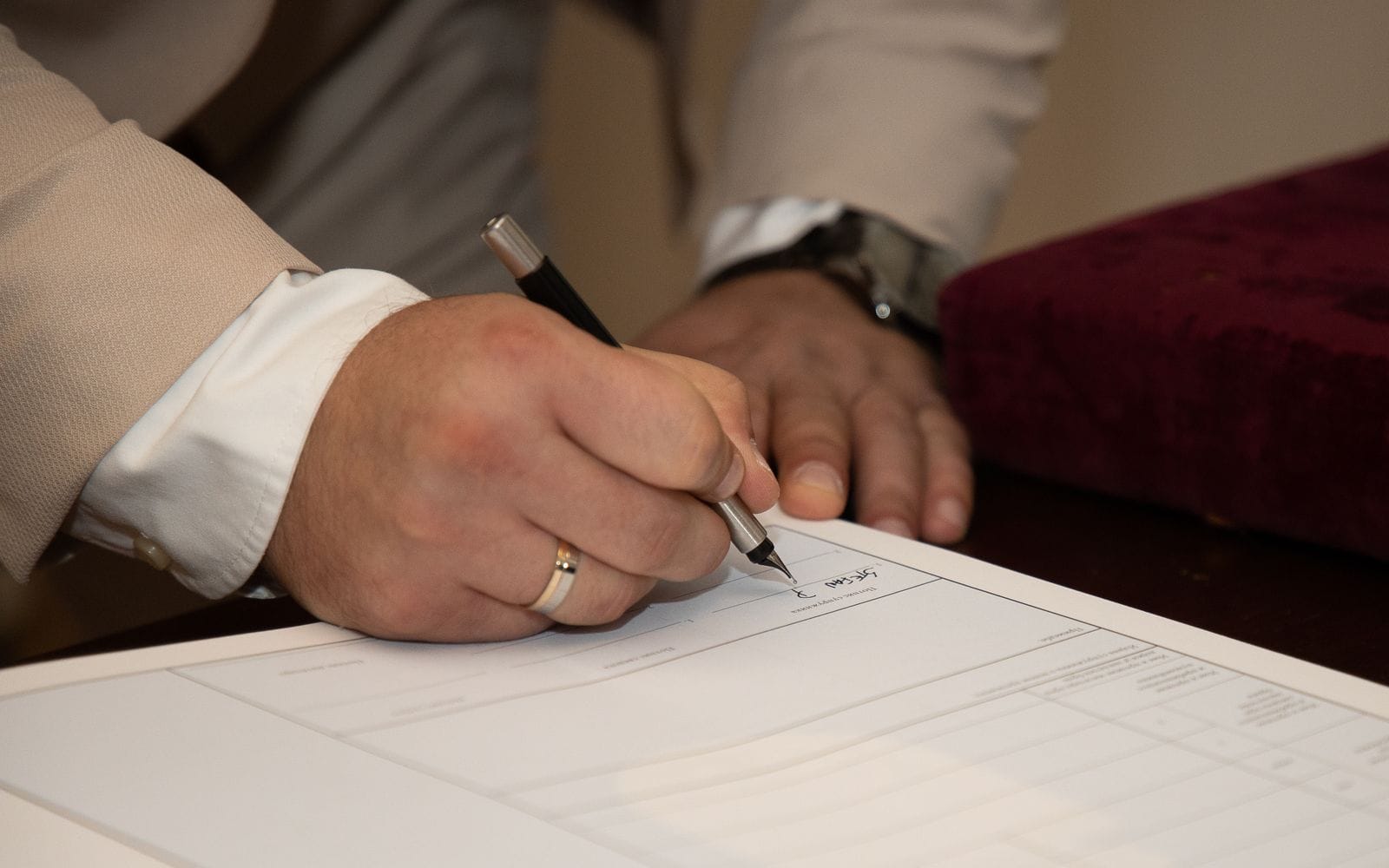 Close-up of a man in a suit signing a printed document with a pen