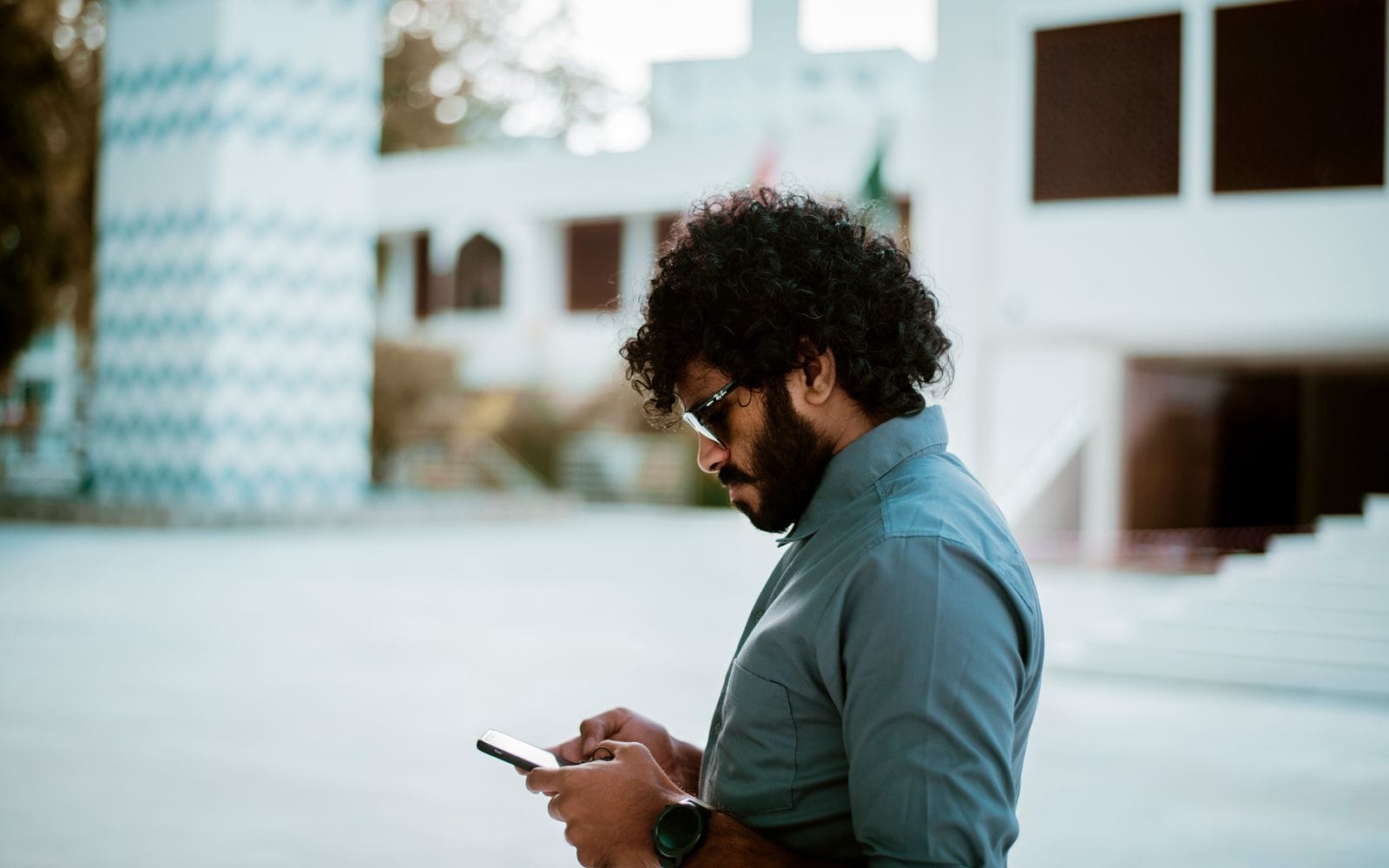 A young man in a green sweater and mustard beanie looking up from his phone