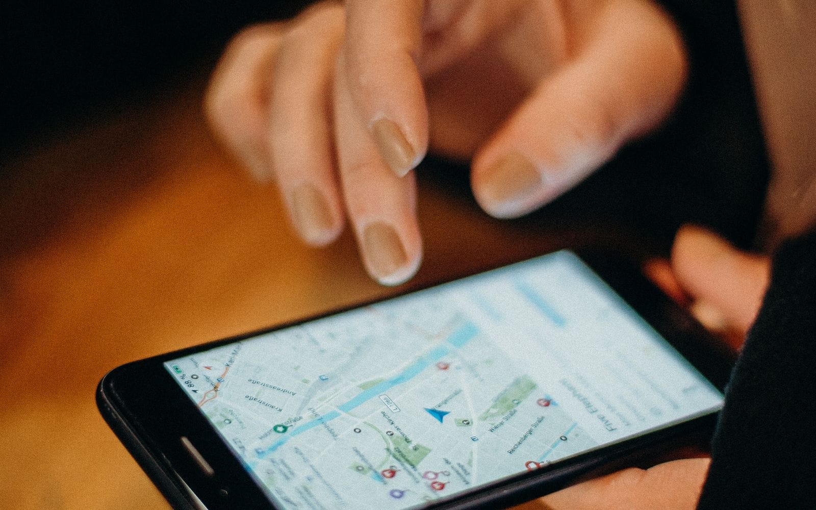 A hand zooming into a map on a smartphone lying on a wooden table