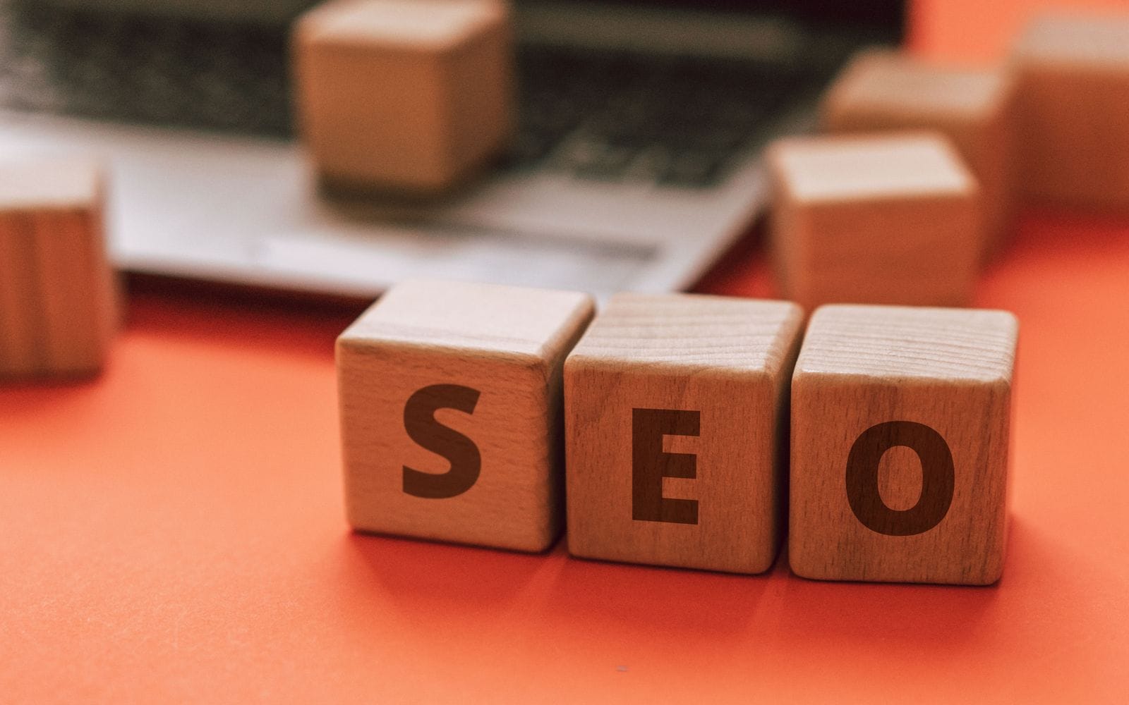 Wooden blocks spelling SEO on an orange surface next to a laptop