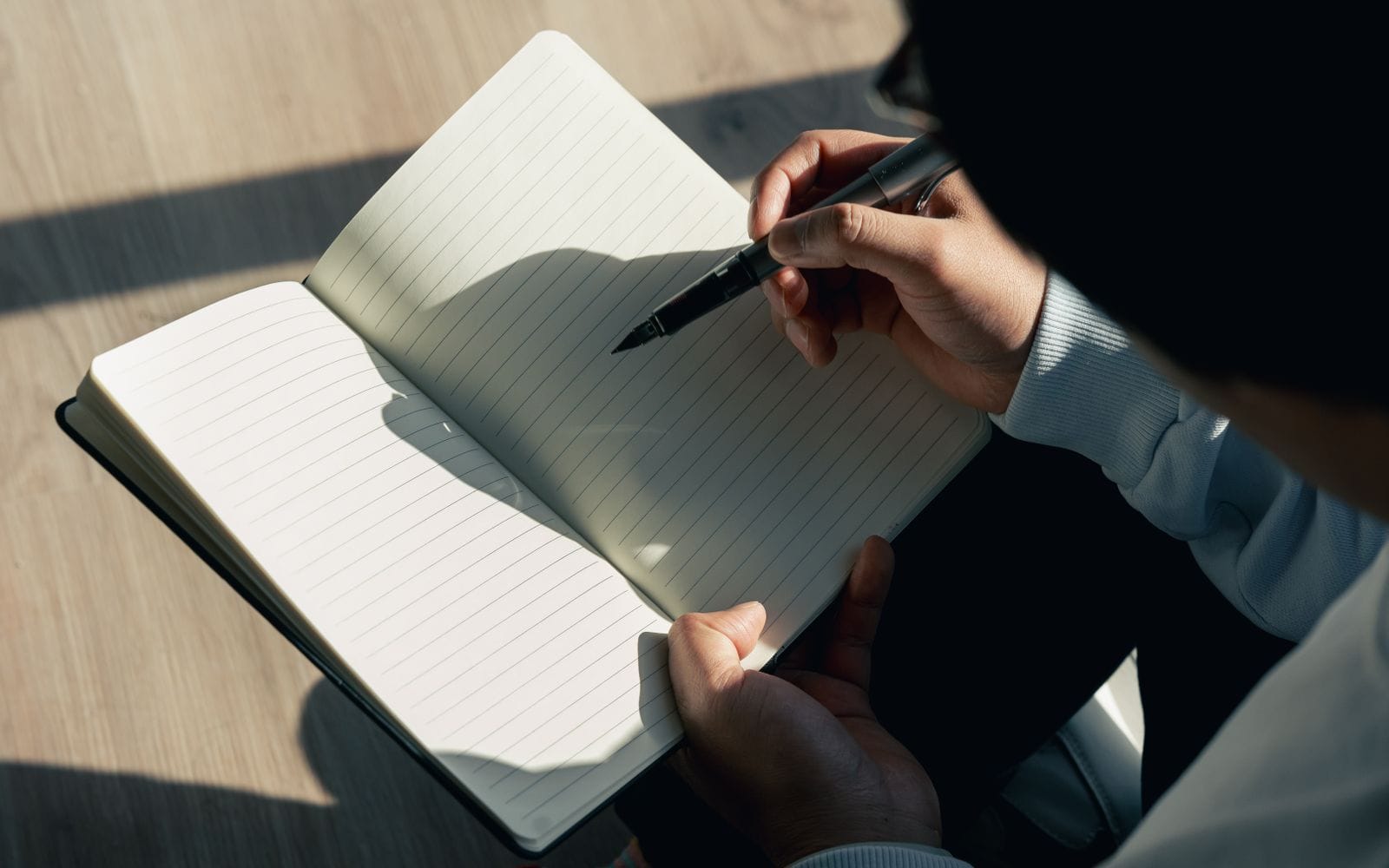 A person in a dark jacket writing in an open notebook on a desk