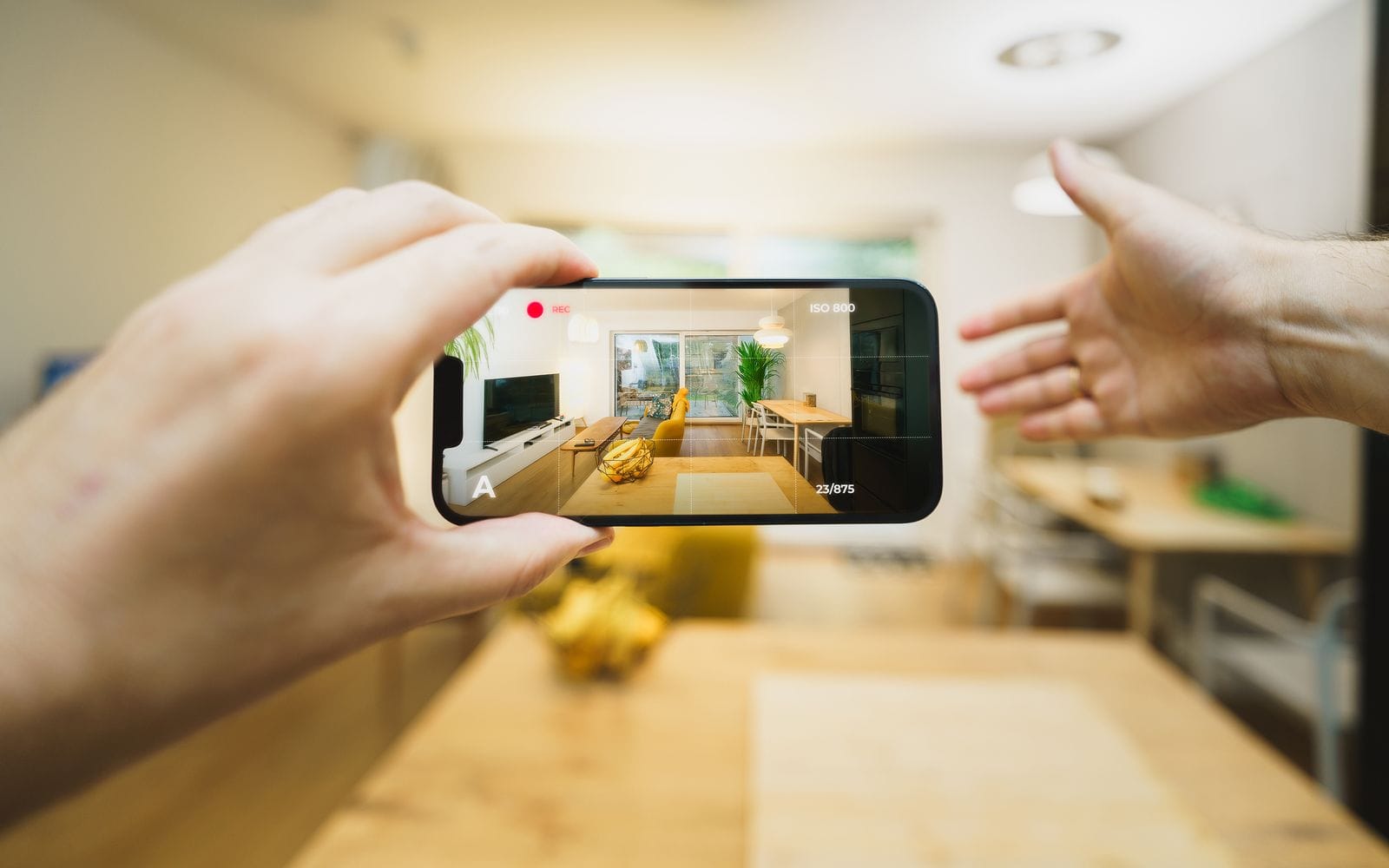 Hands holding a smartphone horizontally to film the living room of a bright apartment