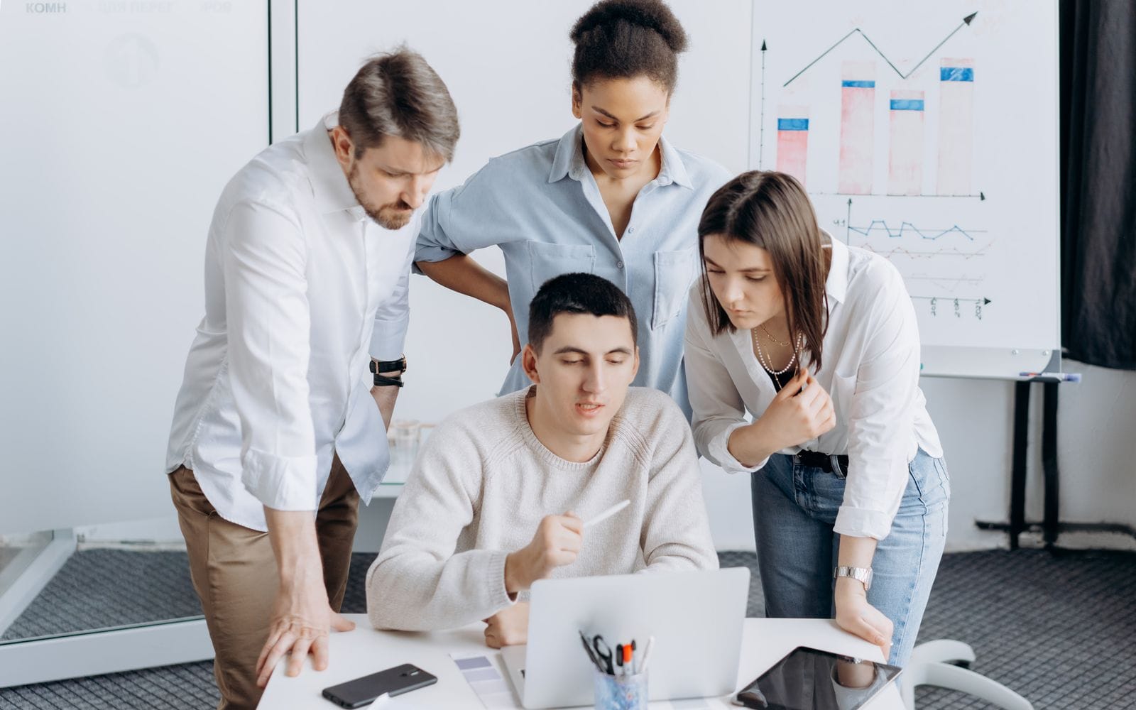 A marketing team gathered around a laptop reviewing results, with charts on a board behind them
