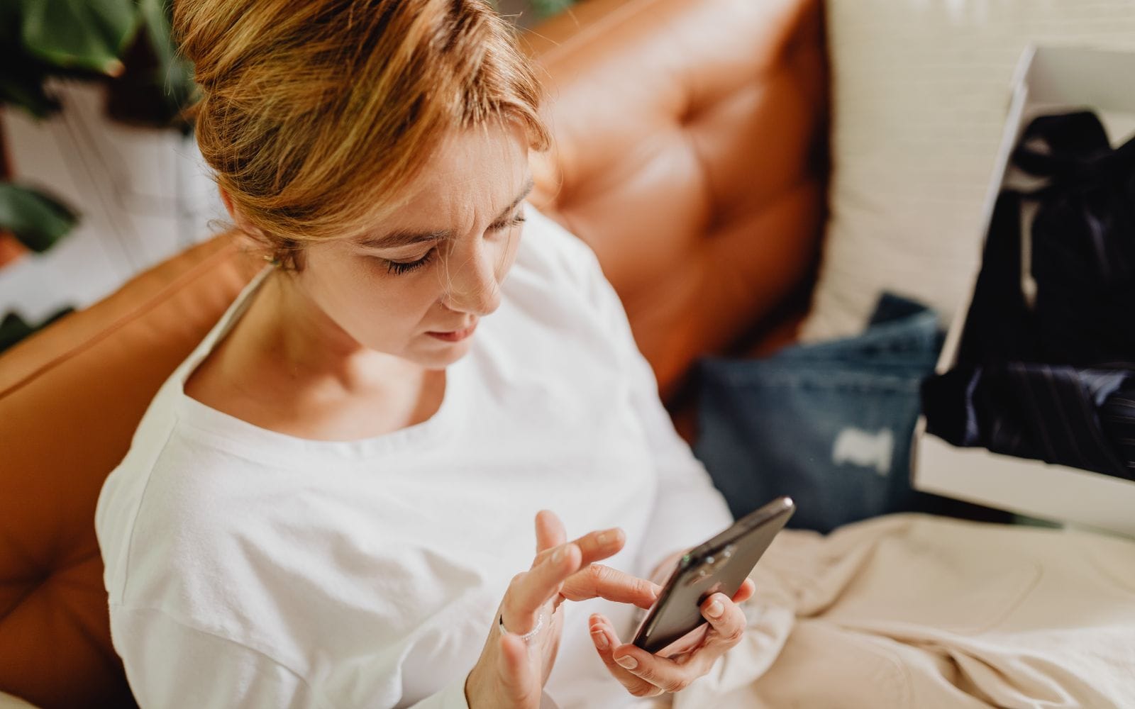 A woman sitting on a sofa typing a message on her smartphone