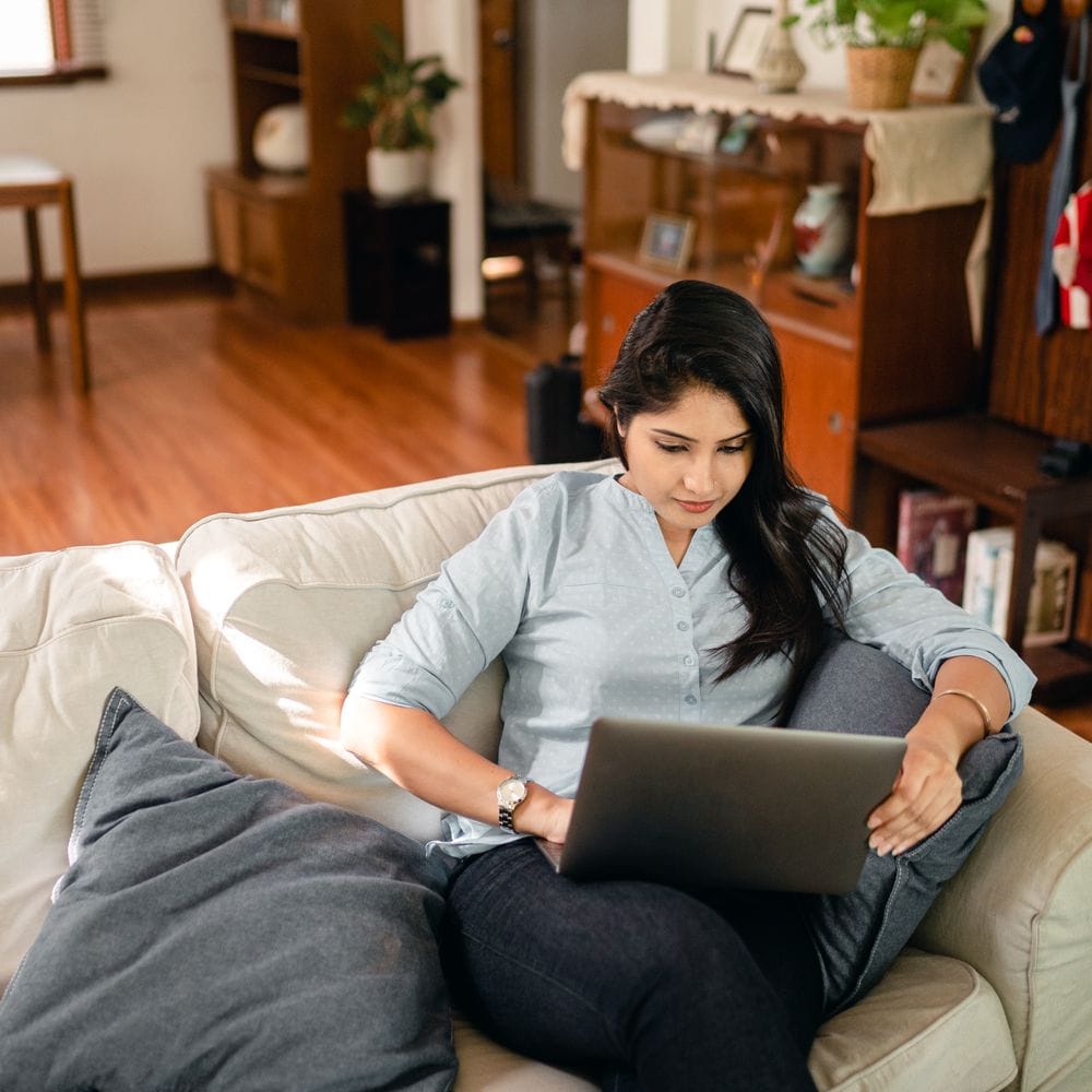 Woman sitting on a sofa at home, browsing on her laptop