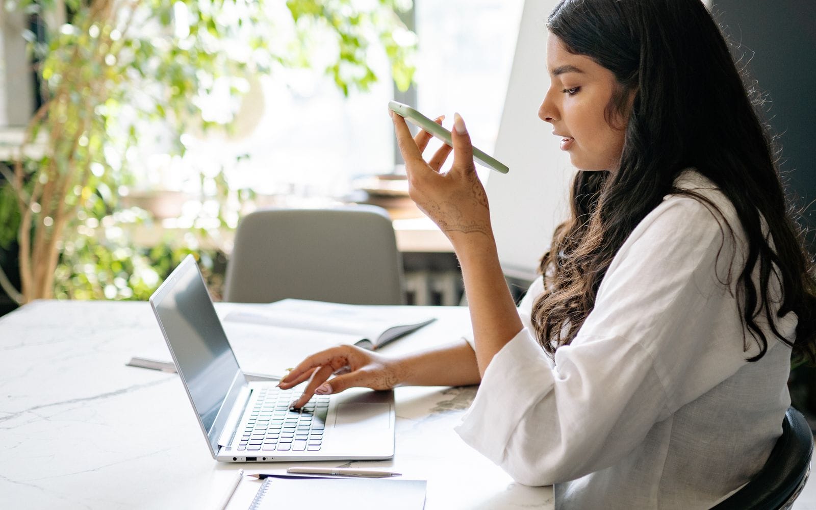 A woman talking on her phone while typing on a laptop at an office desk