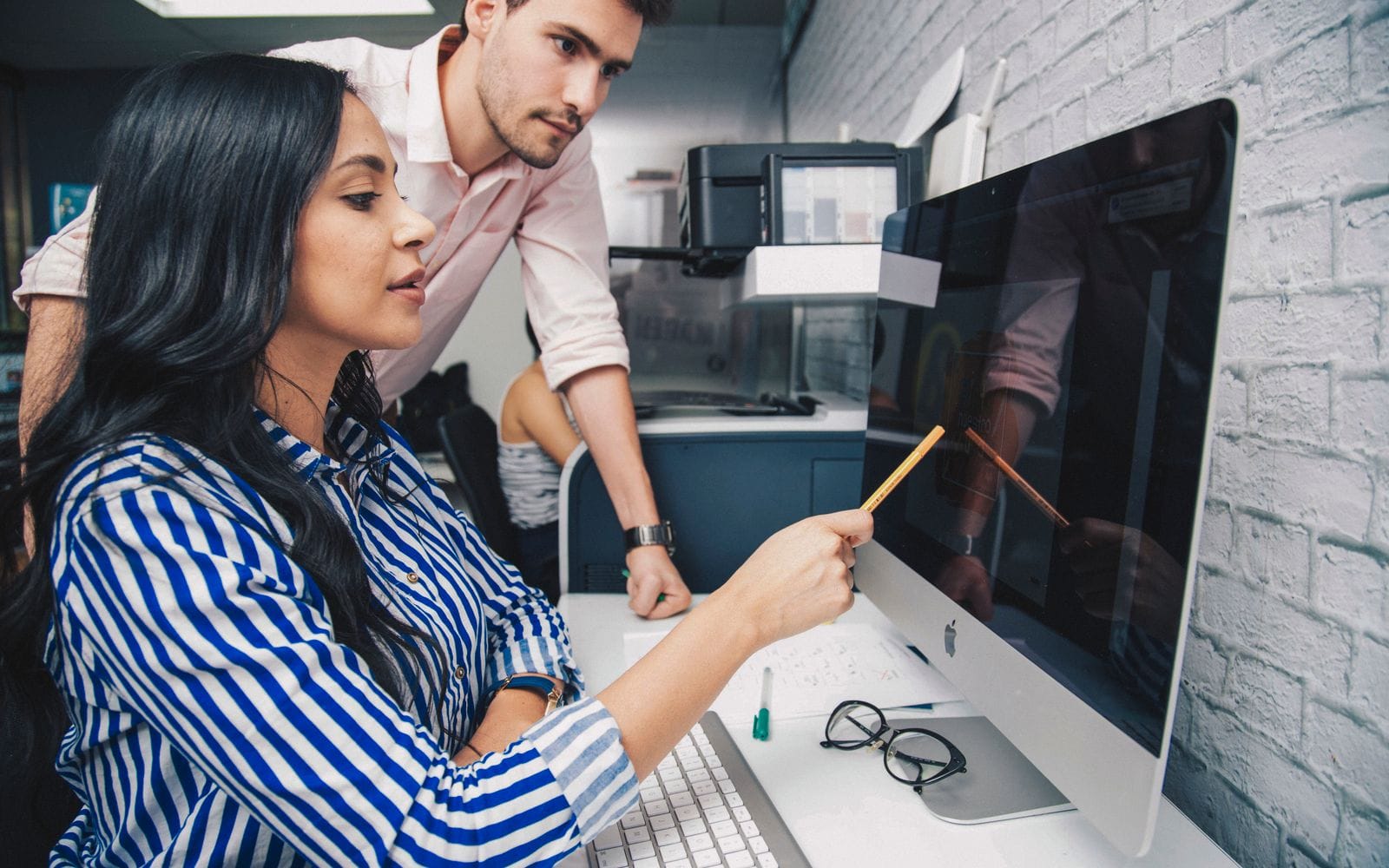 A woman pointing at a computer screen with a pencil while a colleague looks on
