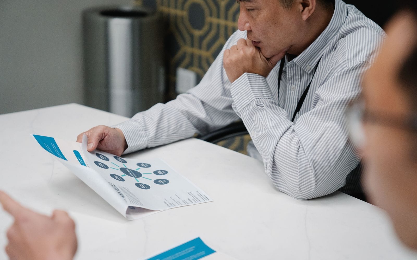 A man in a striped shirt studying a printed leaflet at an office table