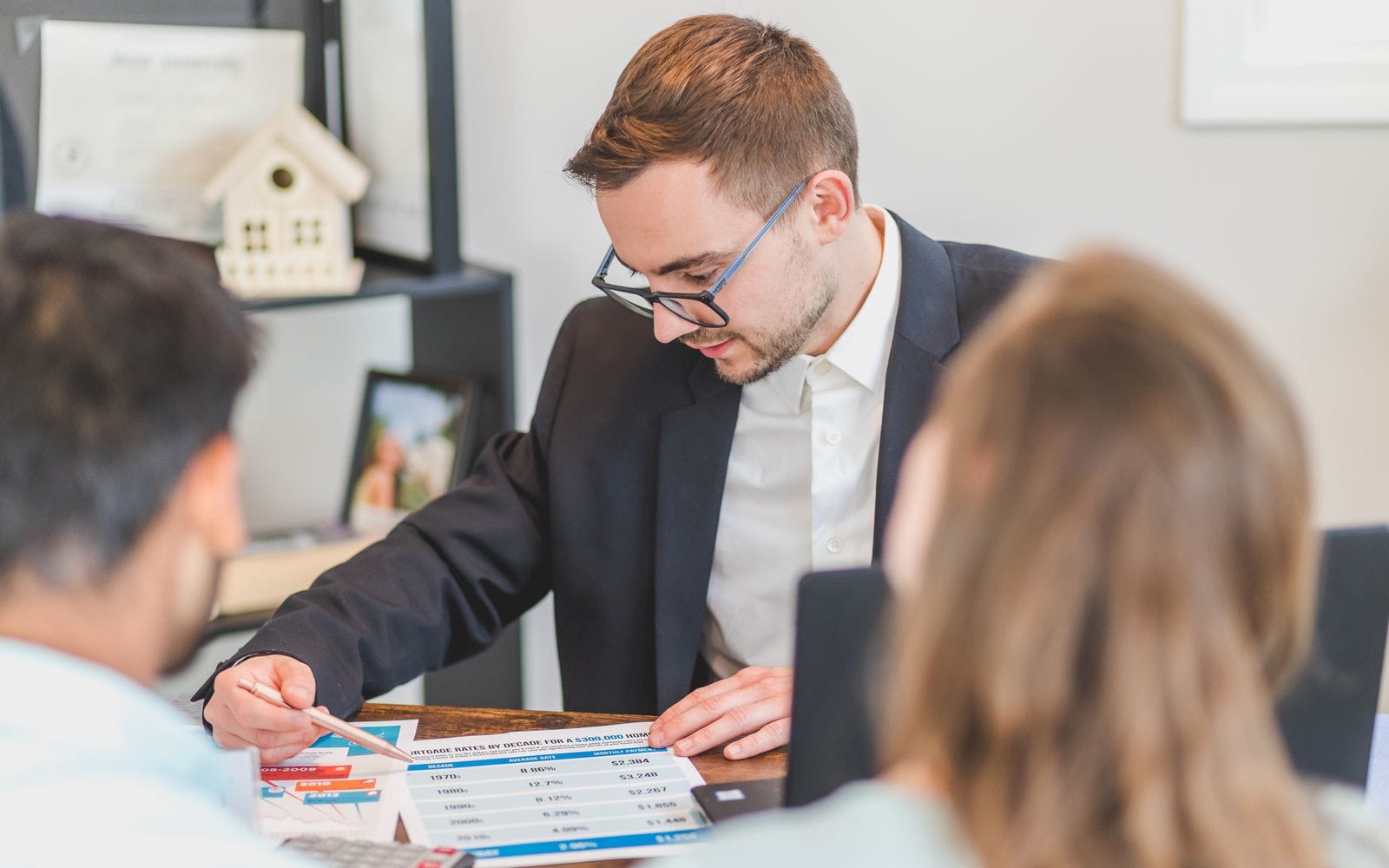 A property advisor explaining figures on a printed sheet to a couple across a desk