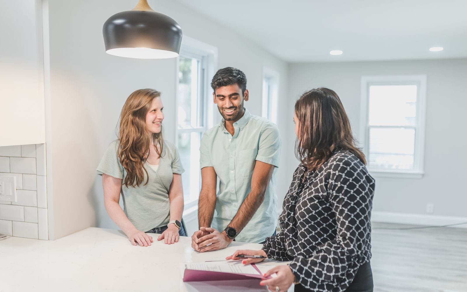 A property executive going over paperwork with a young couple at a kitchen counter