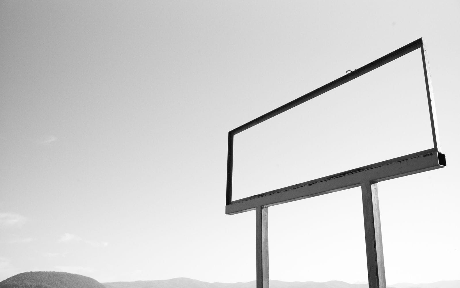 An empty white billboard frame on two posts against a pale grey sky