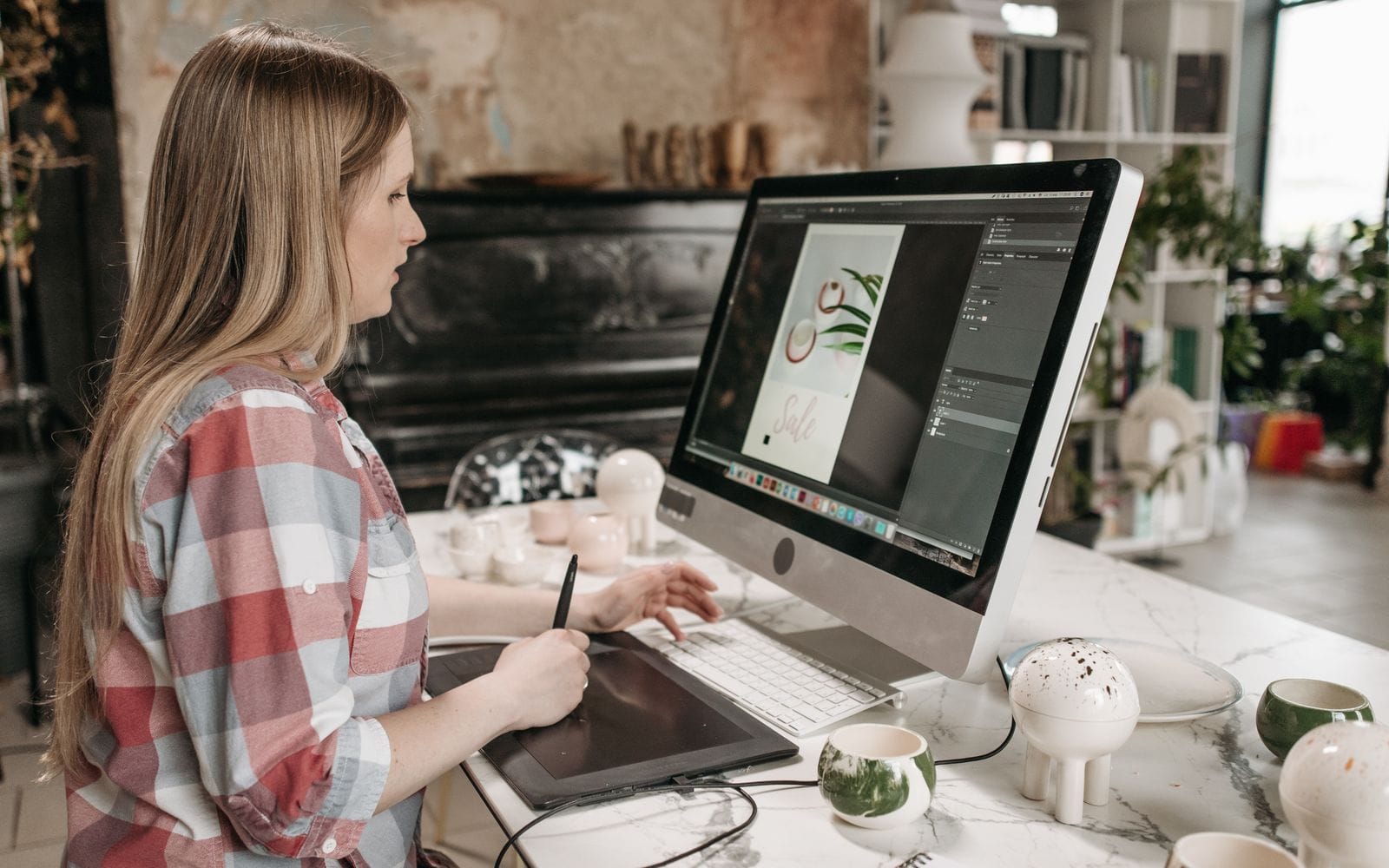 A designer working on a large computer screen with a drawing tablet at her desk