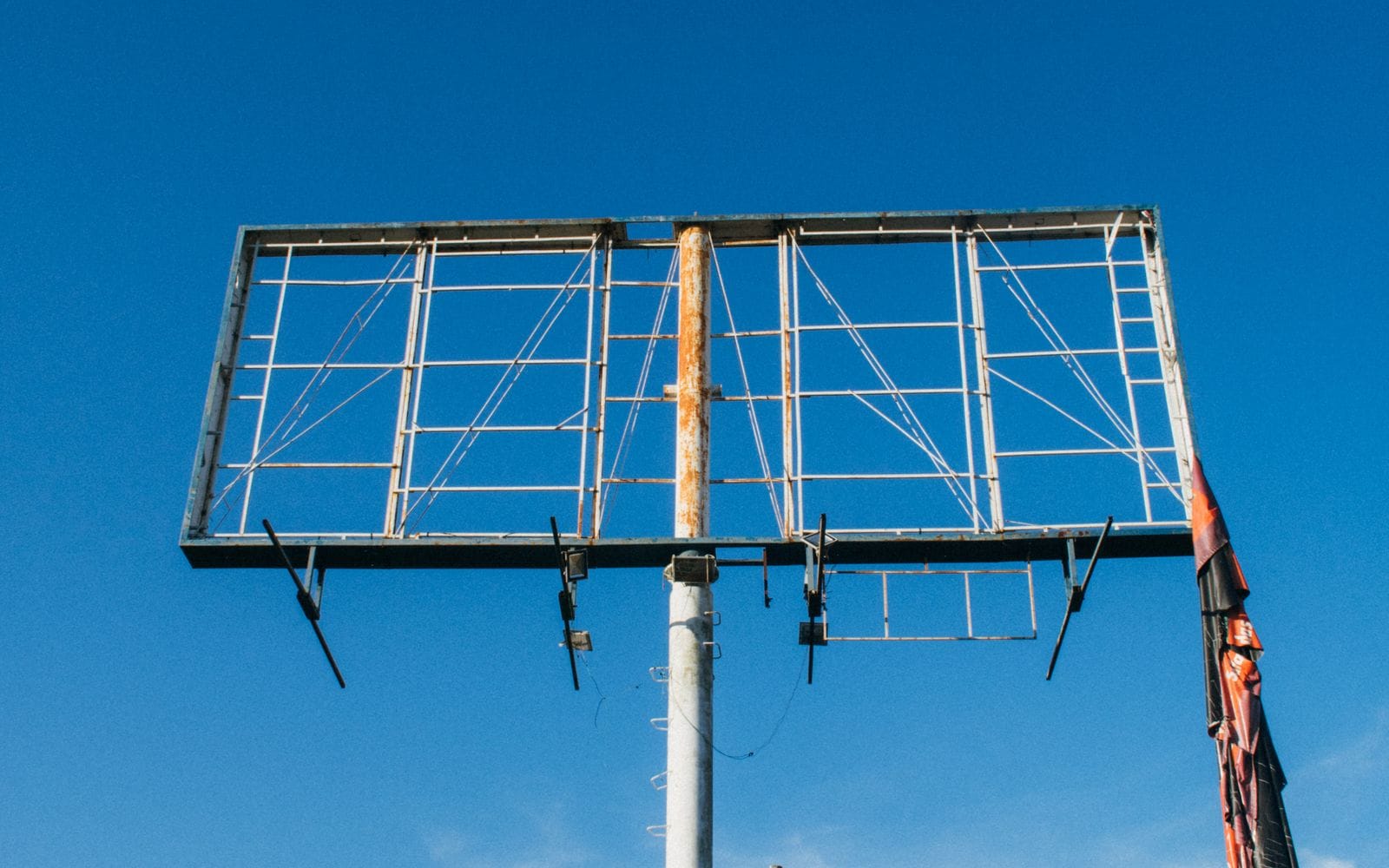 The bare metal frame of a large roadside billboard against a deep blue sky