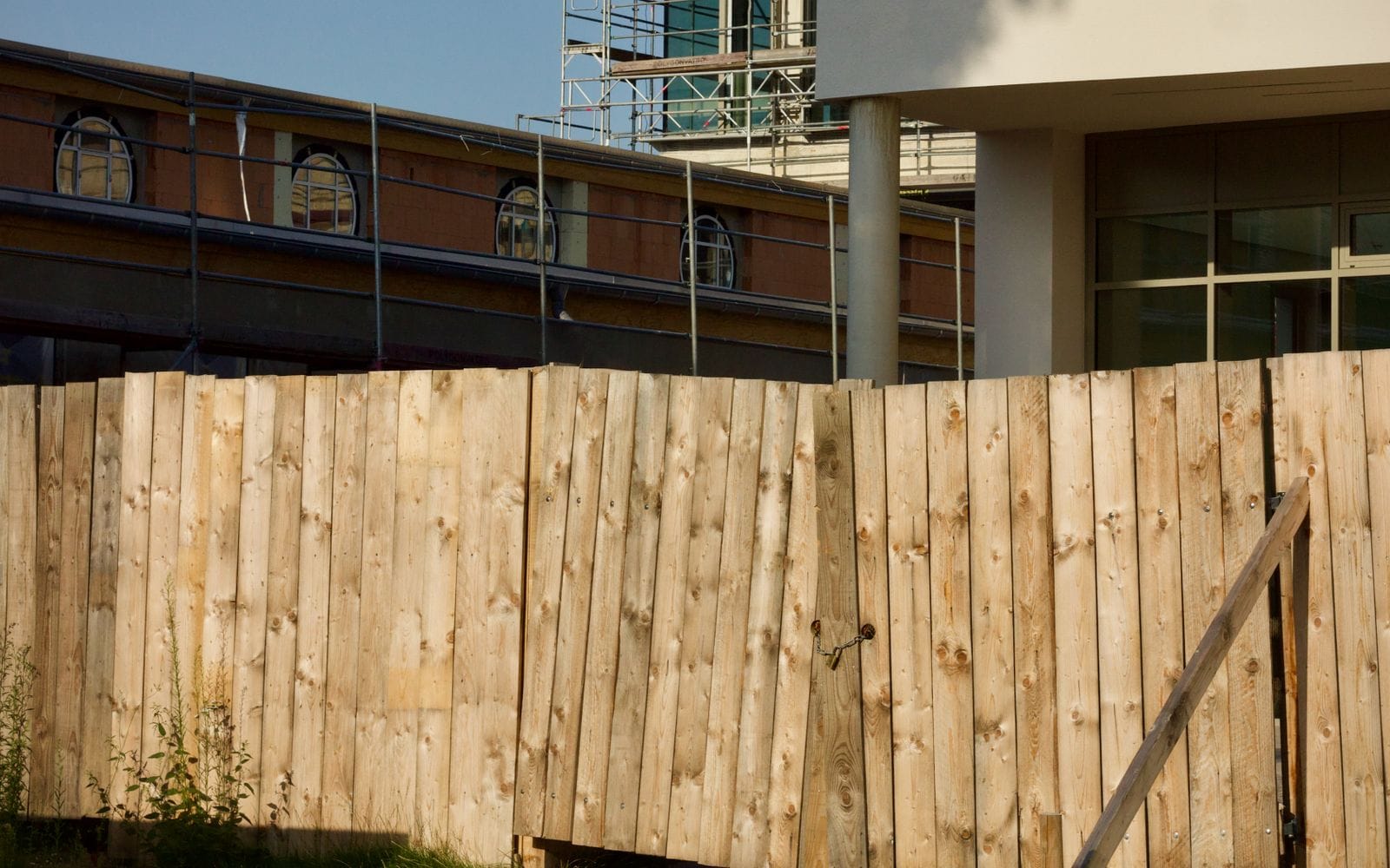 A tall wooden boundary fence around a construction site, with scaffolding behind it