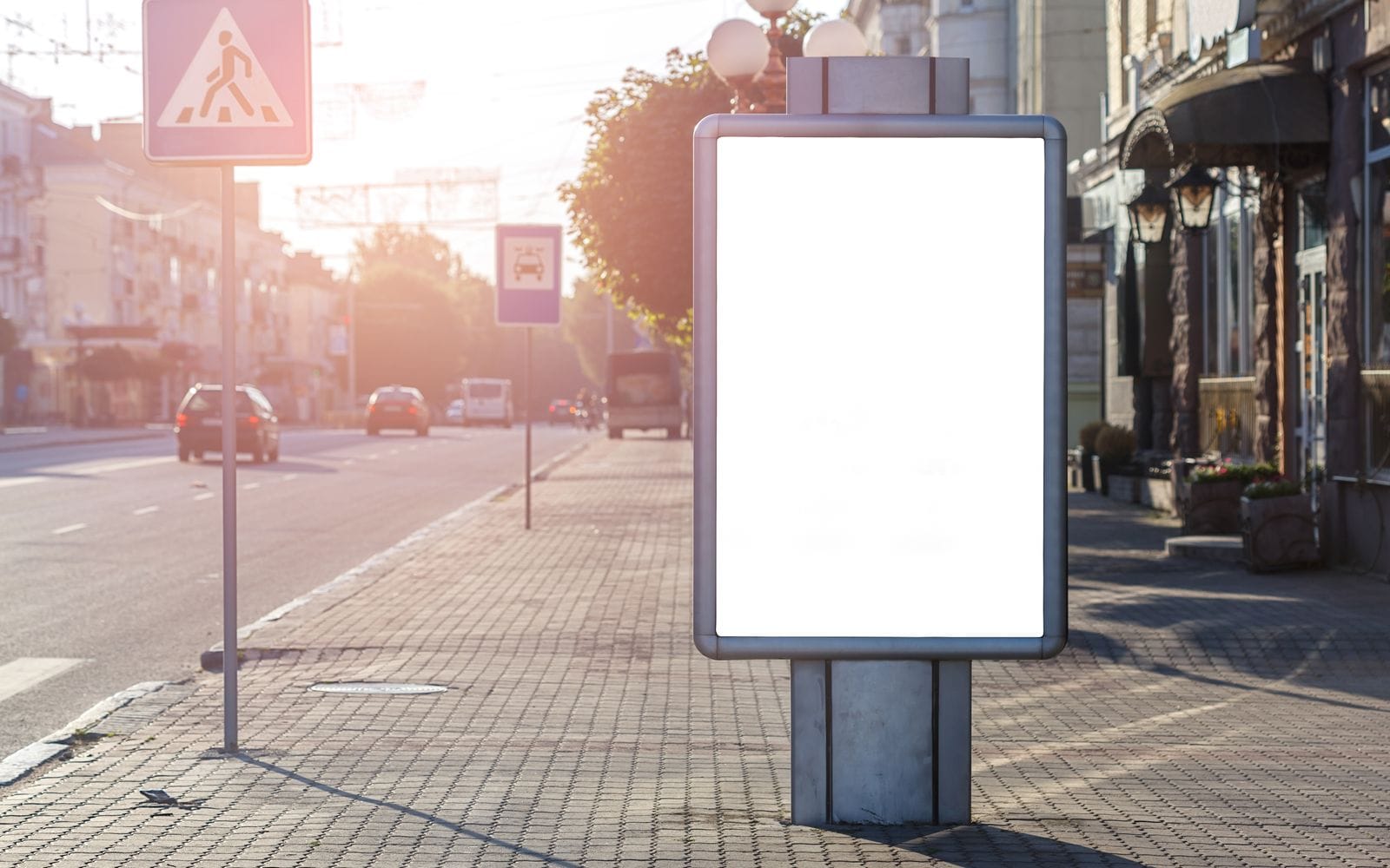A blank lit advertising panel on a pavement beside a sunny street