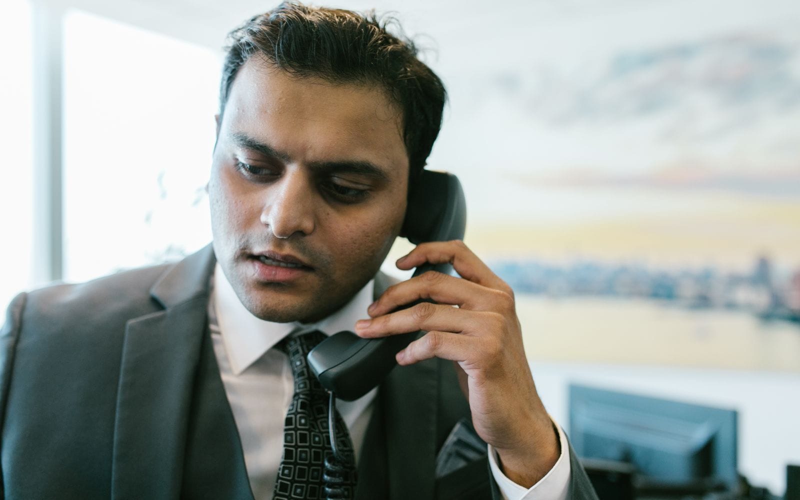 A man in a suit talking on a desk phone in his office
