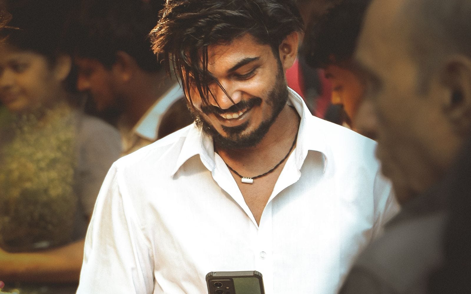 A young man smiling at his phone in a busy market