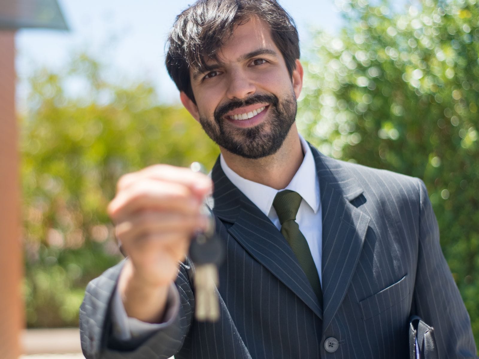 Smiling man in a suit holding out a set of house keys