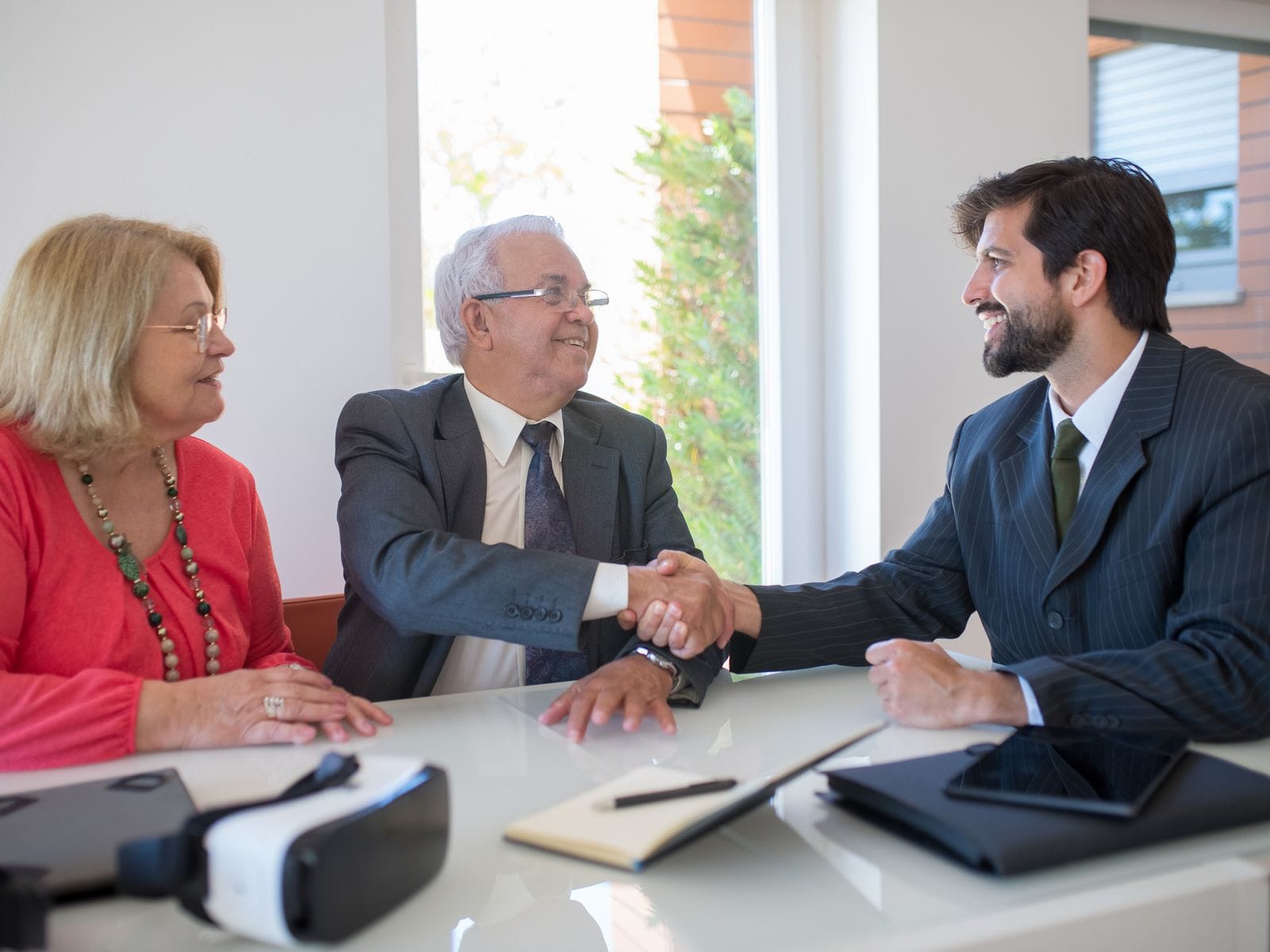 Sales executive shaking hands with an older couple across a desk in a sales office