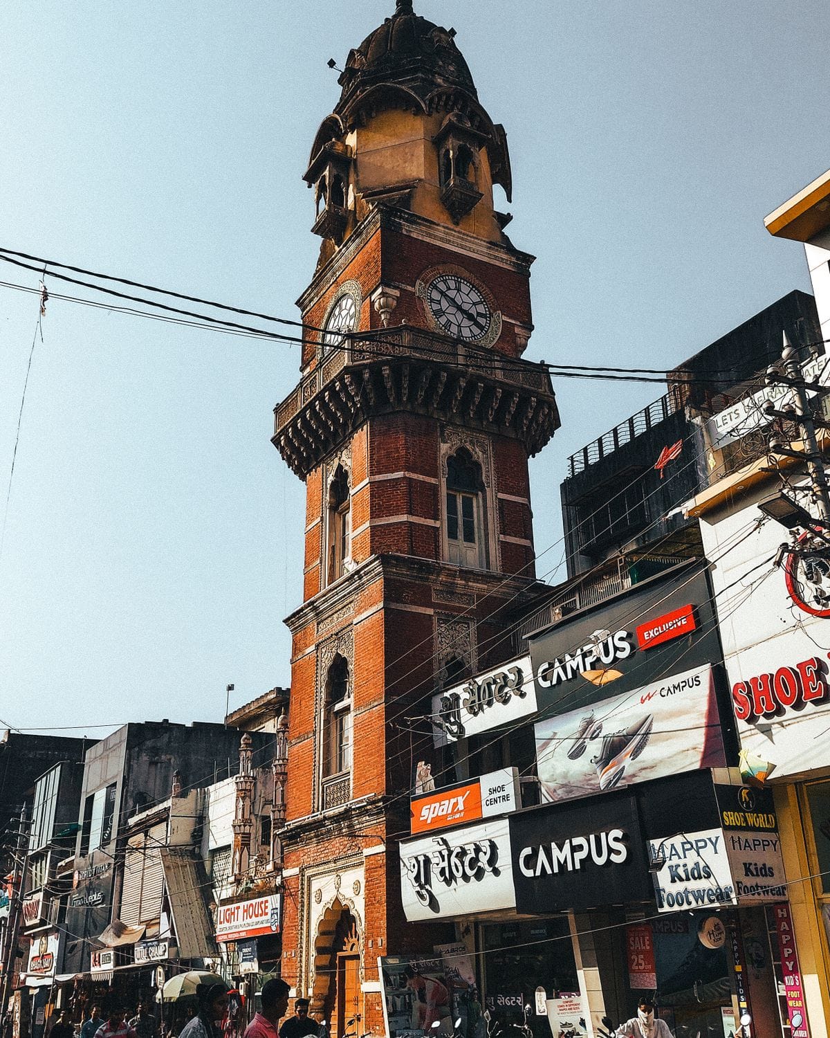 Red-brick clock tower above a busy market street with shop signs