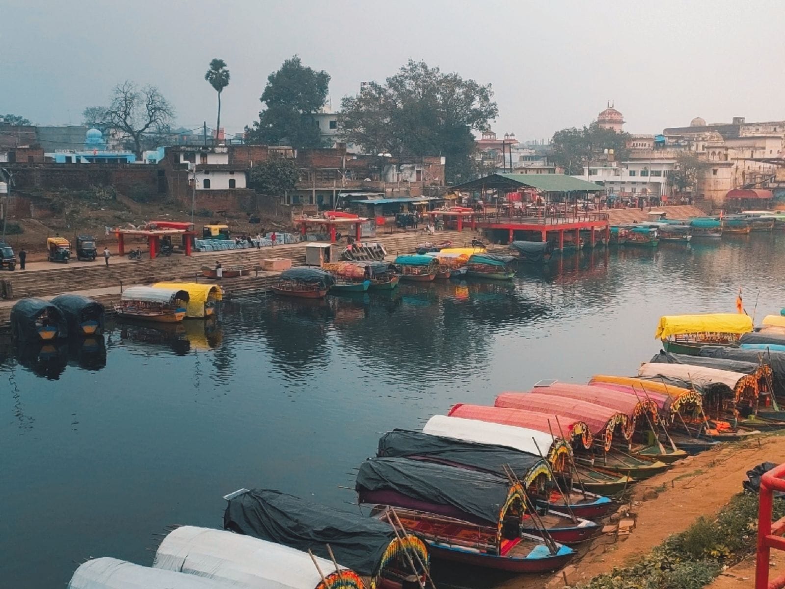 Boats moored along a river bank on a hazy morning, with buildings behind
