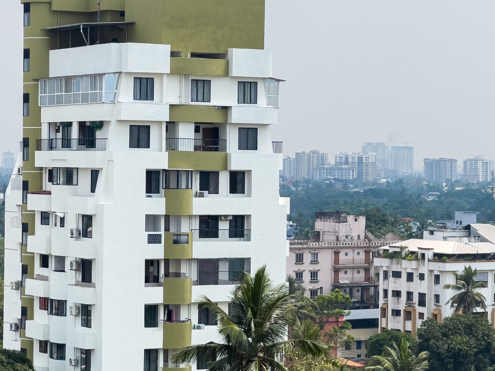 White apartment building with balconies, with the city skyline behind it