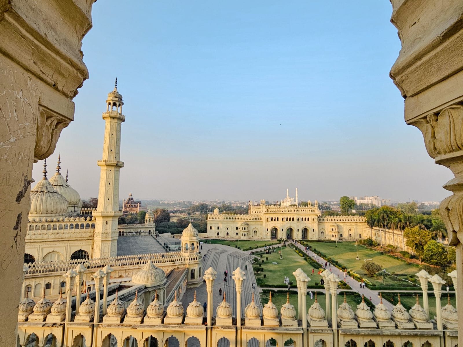 A minaret, gardens and a domed building seen through a carved stone arch