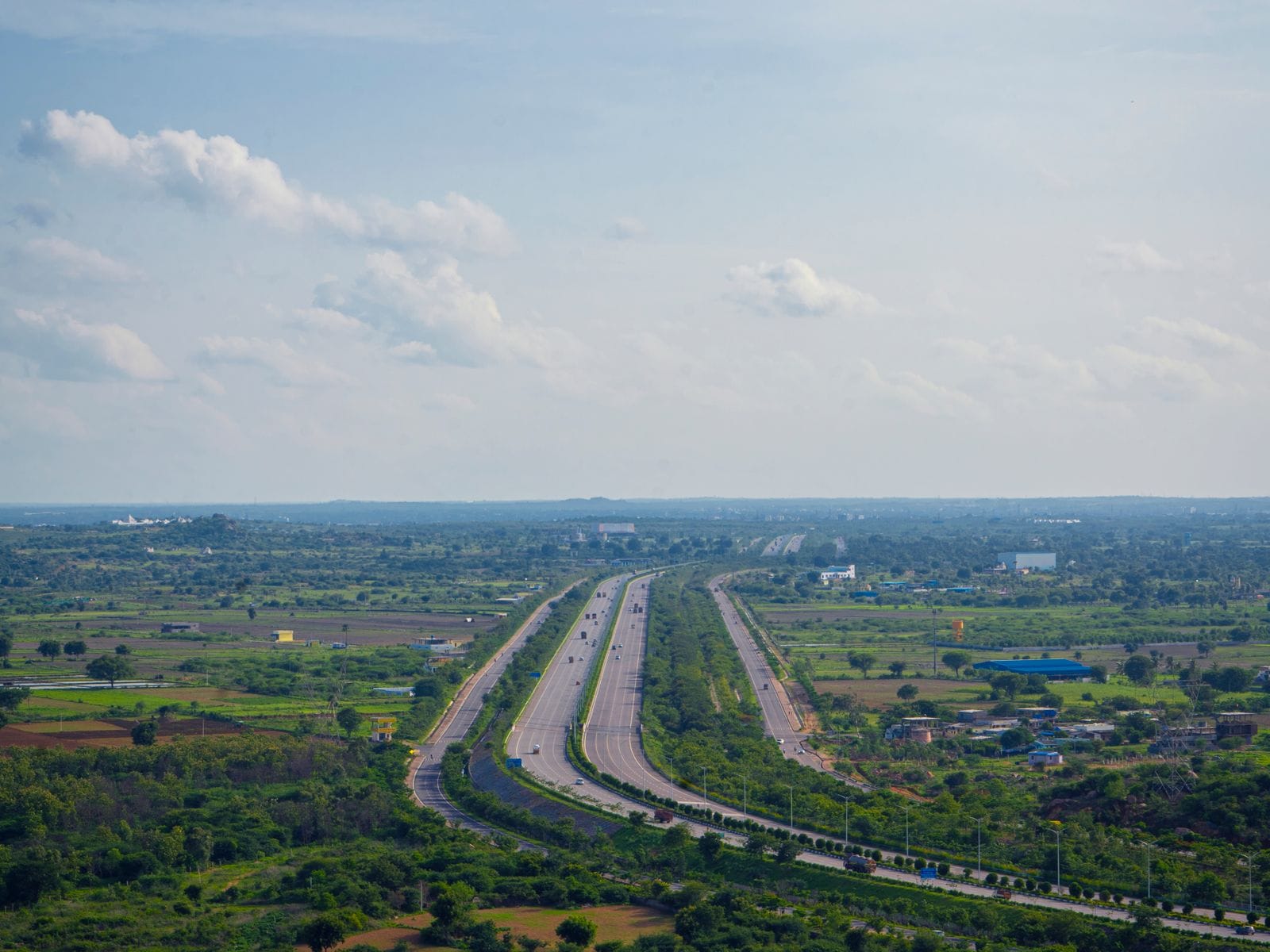 A wide expressway running through green fields towards the horizon