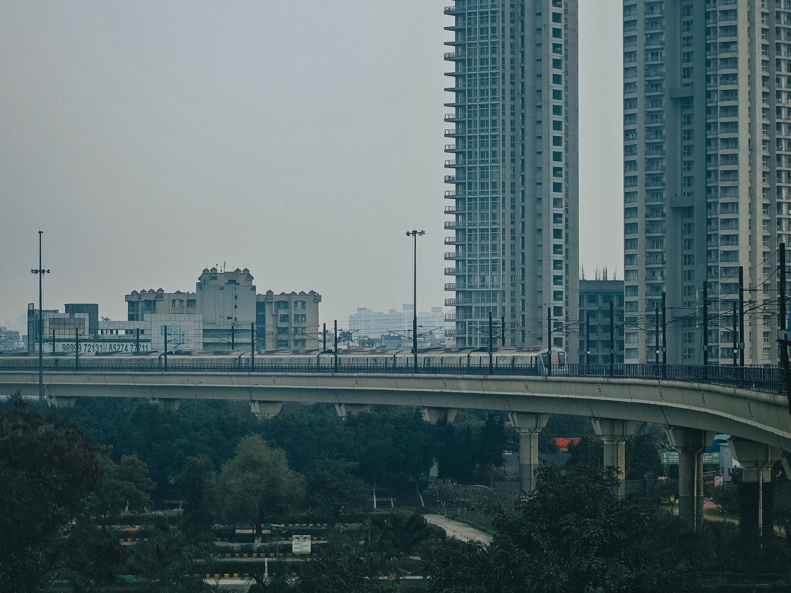 An elevated metro viaduct curving past tall residential towers on a hazy day