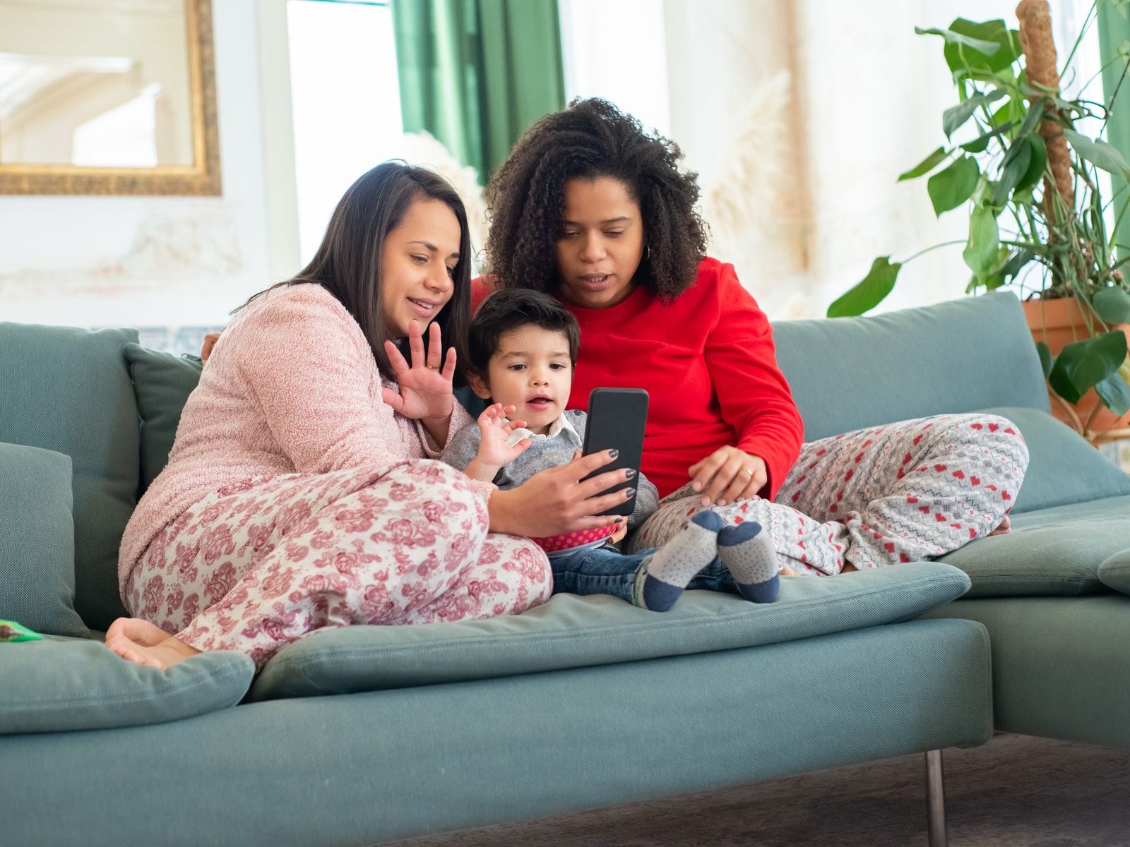 Two women and a small child on a sofa looking at a phone together
