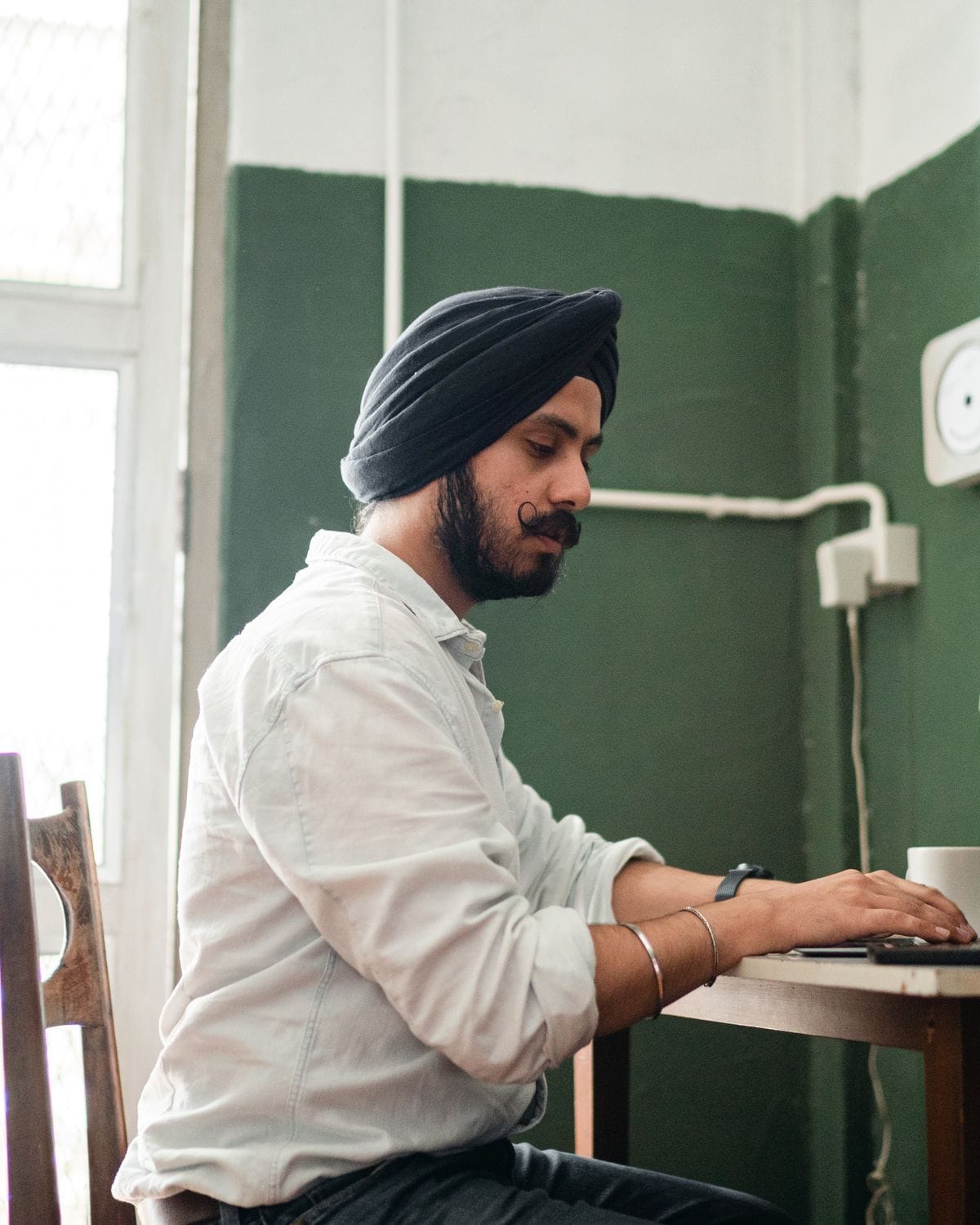 Man in a turban working on a laptop at a small table at home