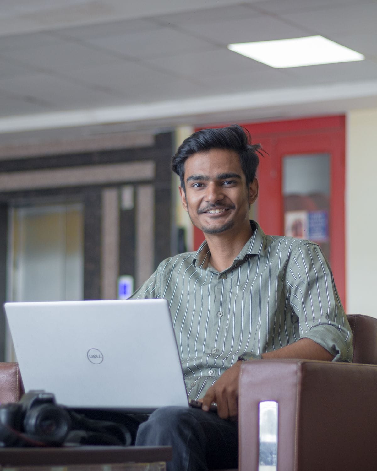 Young man smiling while working on a laptop in a lounge