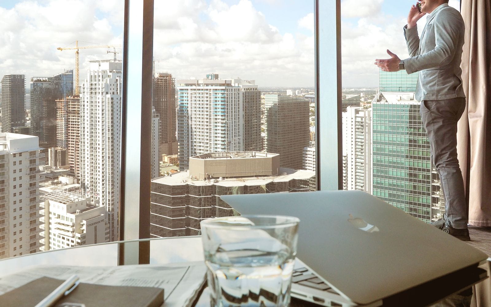 Man on a phone call by the window of a high-rise office overlooking a city