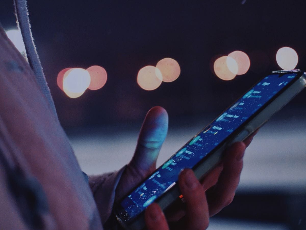 Hand holding a smartphone at night with city lights behind